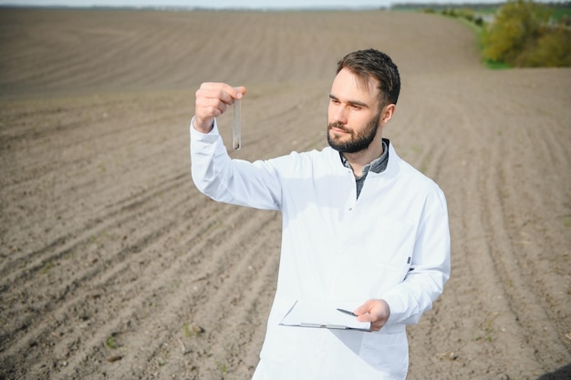 Foto trabalhador de laboratório segurando produtos vidreiros profissionais e testando solo preto após a colheita no campo