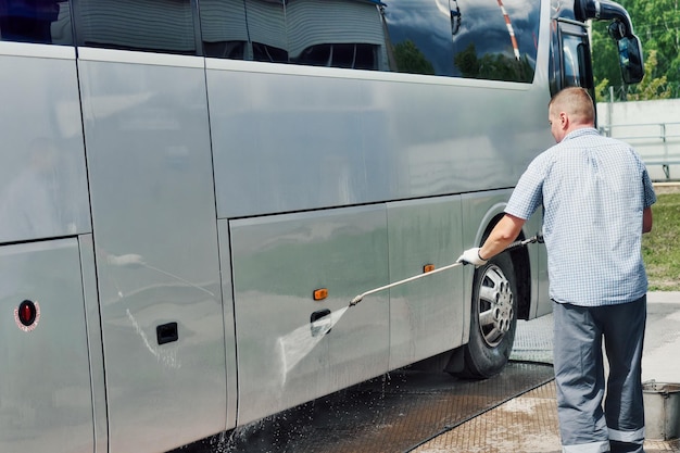 Trabalhador de lavagem de carro lava manualmente grande ônibus com fluxo de água em estacionamento aberto no dia de verão