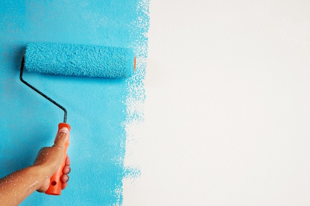 Trabalhador de pintura de pincel de rolo pintando na parede de superfície pintura de apartamento reformando com tinta de cor azul deixe o espaço vazio da cópia em branco para escrever o texto descritivo ao lado