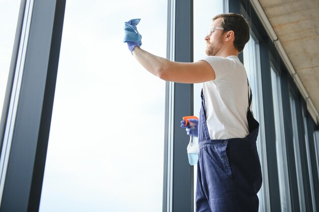 Trabalhador de serviço de limpeza profissional masculino em macacão limpa as janelas e vitrines de uma loja com equipamentos especiais