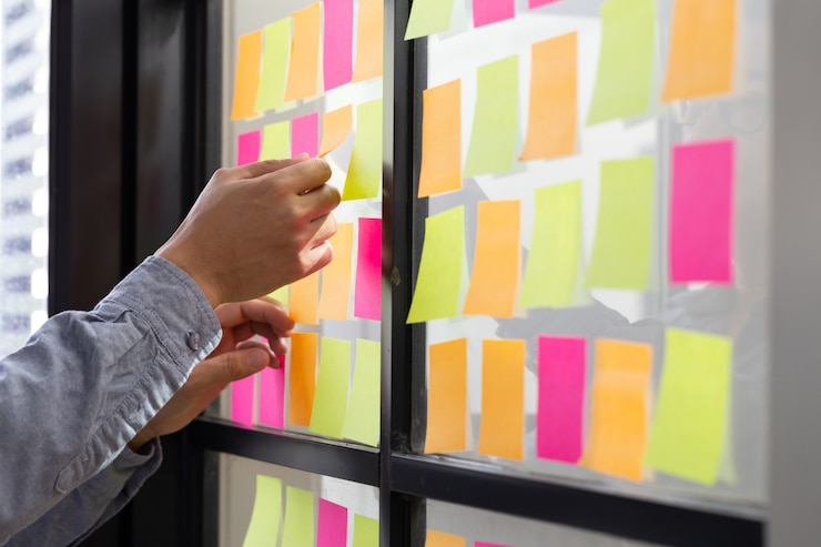 Foto trabalhador de ti, rastreando suas tarefas no quadro kanban. utilizando controle de tarefas da metodologia de desenvolvimento ágil. homem, anexar, nota pegajosa, para, scrum, quadro tarefa, em, a, escritório
