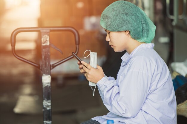 Trabalhador de trabalho jovem birmanês asiático sentar e relaxar, jogando telefones celulares, à espera de turnos de trabalho na fábrica de higiene alimentar.