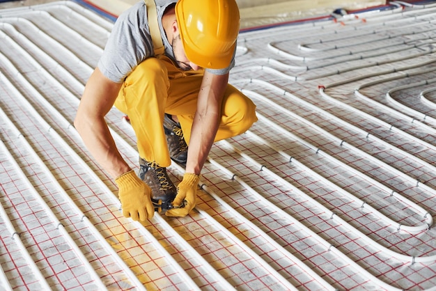 Trabalhador de uniforme de cor amarela instalando sistema de aquecimento por piso radiante