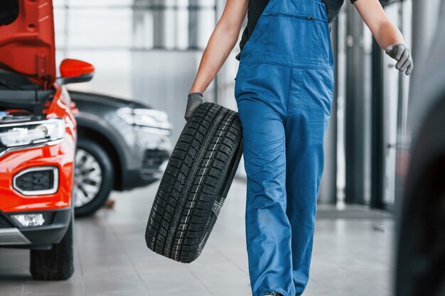 Trabalhador de uniforme preto e azul, segurando a roda do carro e tem trabalho dentro de casa