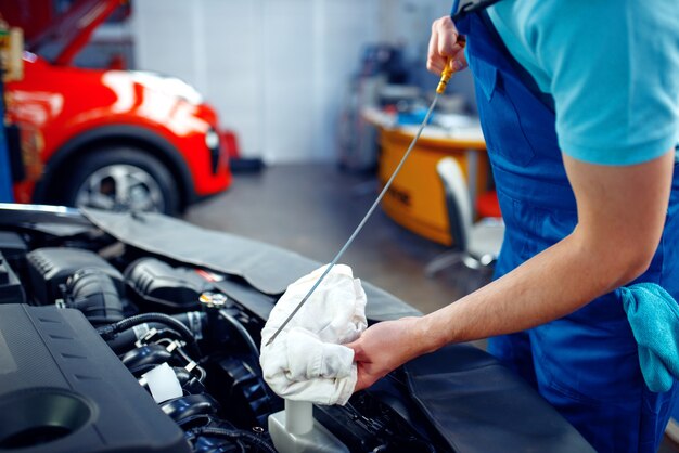 Trabalhador de uniforme verifica o nível de óleo do motor, posto de serviço do carro. Verificação e inspeção de automóveis, diagnósticos profissionais e reparos