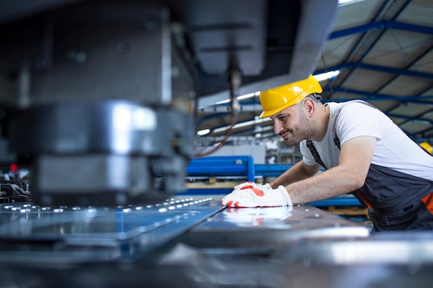 Trabalhador do sexo masculino com equipamento de proteção e capacete de segurança trabalhando na máquina industrial na linha de produção da fábrica.