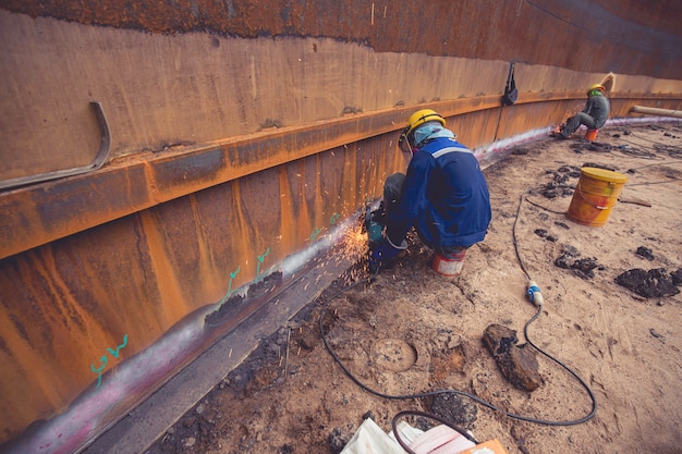 Trabalhador do sexo masculino moendo na placa de aço com flash de faíscas perto de usar luvas de proteção de óleo dentro de espaços confinados.