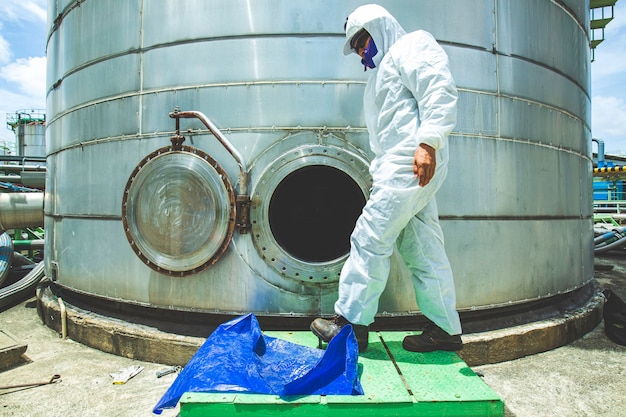 Trabalhador do sexo masculino no poço de inspeção de óleo do tanque de combustível, área de roupas de proteção química, espaço confinado perigoso