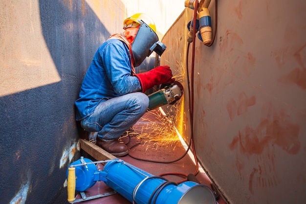 Trabalhador do sexo masculino usando roupas de proteção e reparando a placa inferior do tanque de armazenamento de moagem dentro de espaços confinados