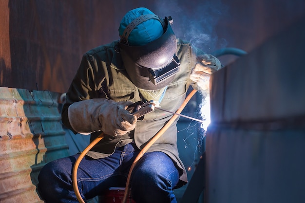 Foto trabalhador do sexo masculino vestindo roupas de proteção e óleo de tanque de placa de reparo soldagem construção industrial dentro de espaços confinados.