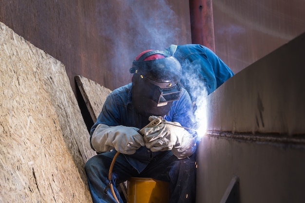 Trabalhador do sexo masculino vestindo roupas de proteção e reparo de óleo de construção industrial de soldagem e gás ou tanque de armazenamento dentro de espaços confinados