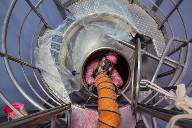 Trabalhador do sexo masculino, vista de cima, subindo as escadas para o tanque, área de produtos químicos em espaço confinado, ventilador de segurança ar fresco