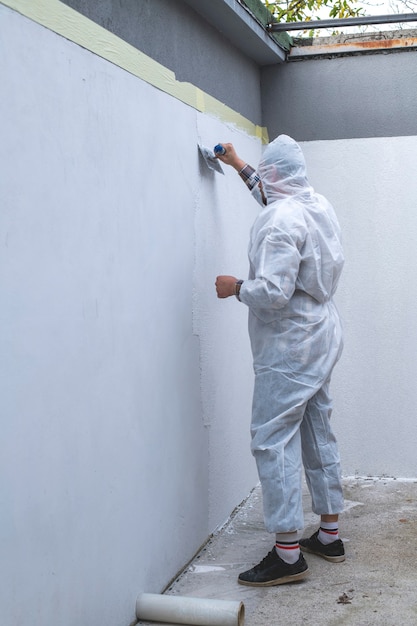 Trabalhador em macacão de proteção branco está rebocando a parede