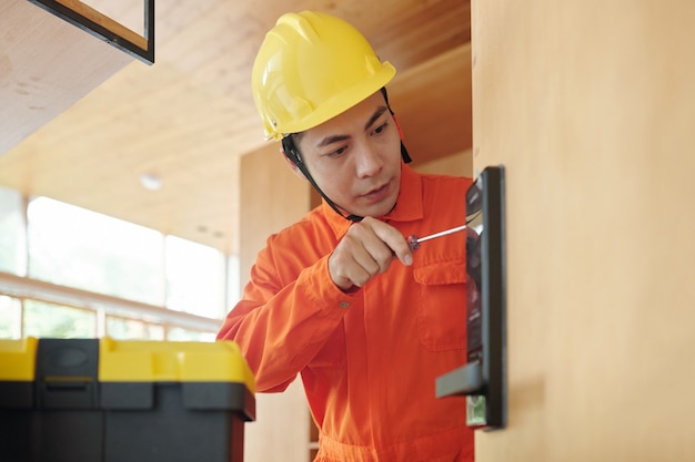 Trabalhador em macacão e capacete instalando fechadura eletrônica inteligente para proteção da casa