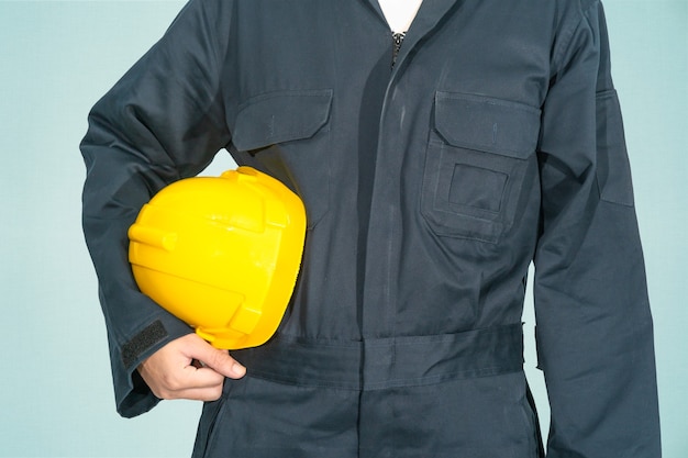 Trabalhador em um macacão azul segurando um capacete de segurança amarelo isolado no fundo azul