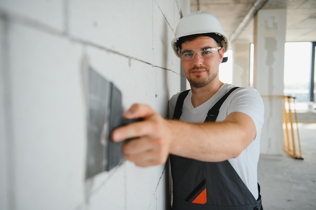 Trabalhador em uniforme de gesso de parede com faca de massa em ambientes fechados