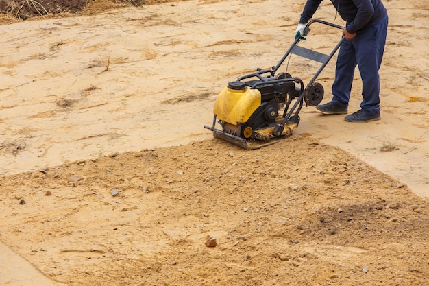 Foto trabalhador em uso compactador de placa vibratória para construção de caminho compactador de placa para compactação de areia equipamento industrial com motor de combustão