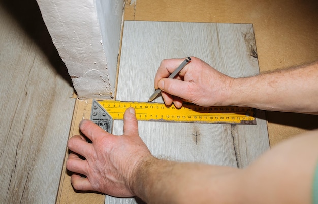 Trabalhador fazendo piso laminado no apartamento Medir fita e lápis nas mãos Renovação de reparos de manutenção Pranchas de parquet de madeira dentro de casa