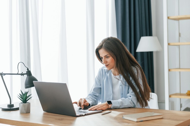 Trabalhador freelancer está sentado à mesa com laptop Jovem mulher bonita está sozinha em casa na sala de casa