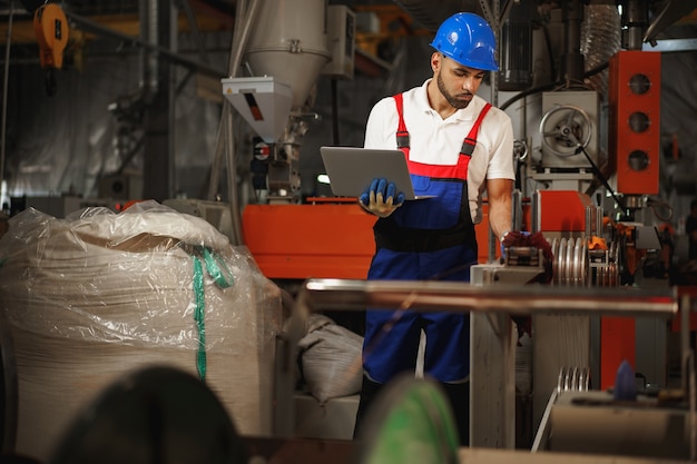 Trabalhador industrial com laptop trabalhando em uma planta de produção de cabos