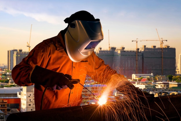 Trabalhador industrial que solda a estrutura de aço com canteiro de obras de prédio alto