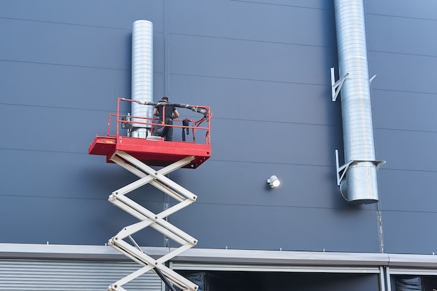 Trabalhador instala um sistema de ventilação na fachada de um edifício usando um elevador de tesoura