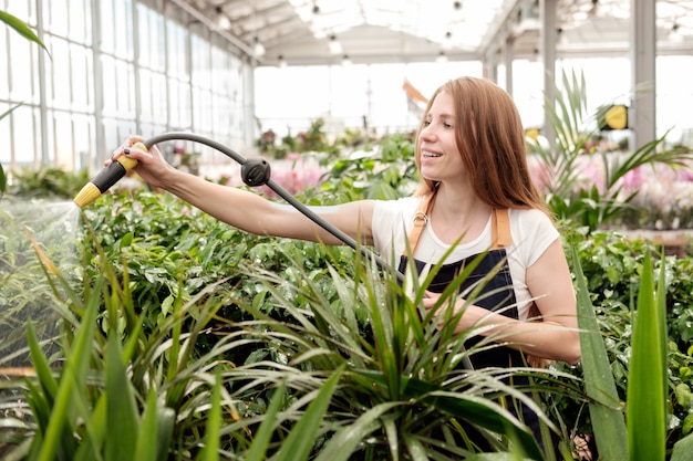 Trabalhador jovem ruiva na estufa do mercado de plantas derramando plantas e sorrindo