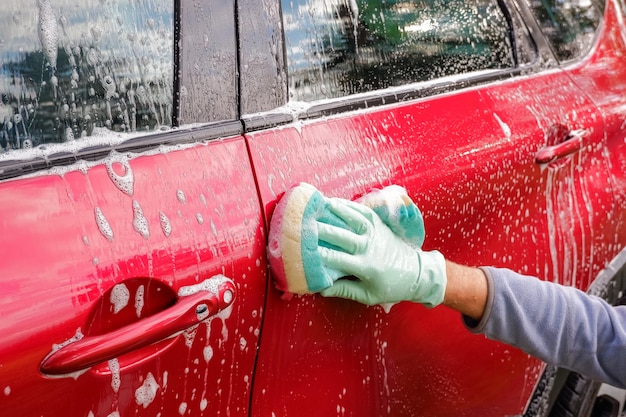 Trabalhador lavando carro vermelho com esponja em um carro de lavagem de mão segura com esponja vermelha verde lavando carro Conceito de lavagem de carro limpoLavando com sabão