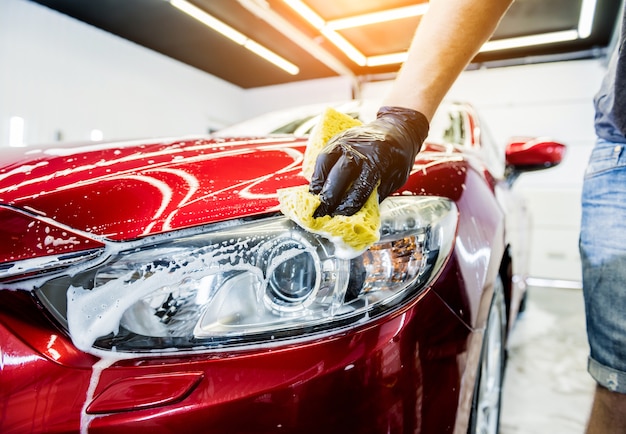 Trabalhador lavando carro vermelho com esponja em uma lavagem de carro.