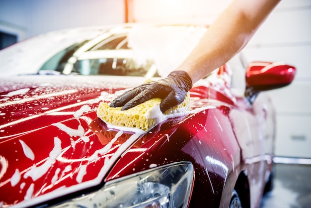 Trabalhador lavando carro vermelho com esponja em uma lavagem de carro.