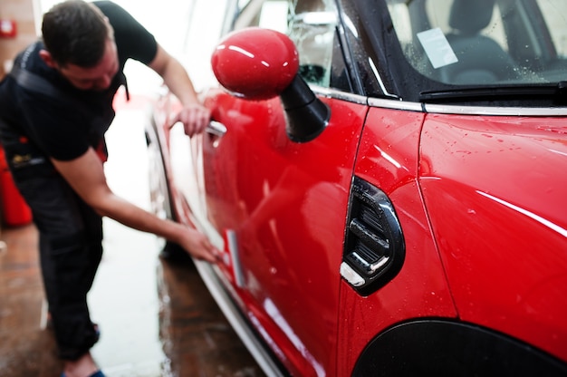 Trabalhador lavando carro vermelho na garagem de detalhamento