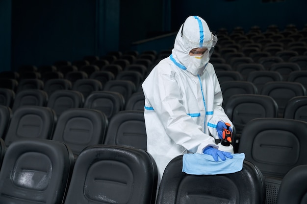 Trabalhador limpando cadeiras no cinema com pano