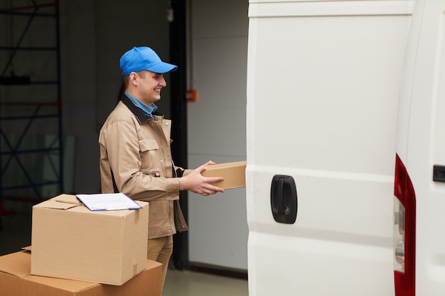 Trabalhador manual carregando caixas e carregando-as na van no armazém