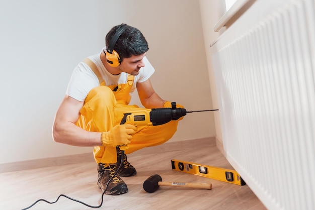 Trabalhador manual de uniforme amarelo trabalha dentro de casa usando broca de martelo Concepção de renovação de casa