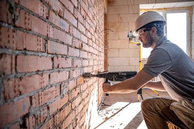 Trabalhador manual em um canteiro de obras no processo de perfuração de uma parede com um perfurador