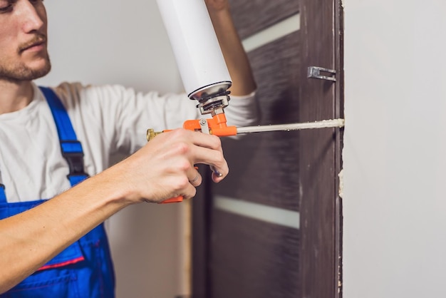 Trabalhador manual jovem instalando a porta com uma espuma de montagem em uma sala.