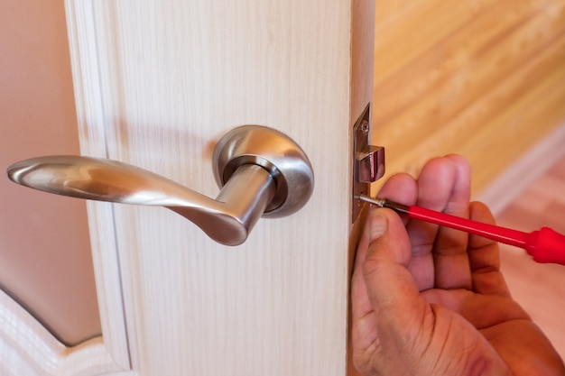 Trabalhador manual repara a fechadura da porta na sala, Homem que fixa a fechadura com uma chave de fenda, Close-up da porta de reparo, serralheiro profissional instalando.