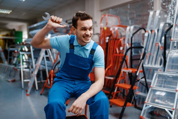 Trabalhador masculino de uniforme sorridente segurando a chave inglesa na loja de ferramentas