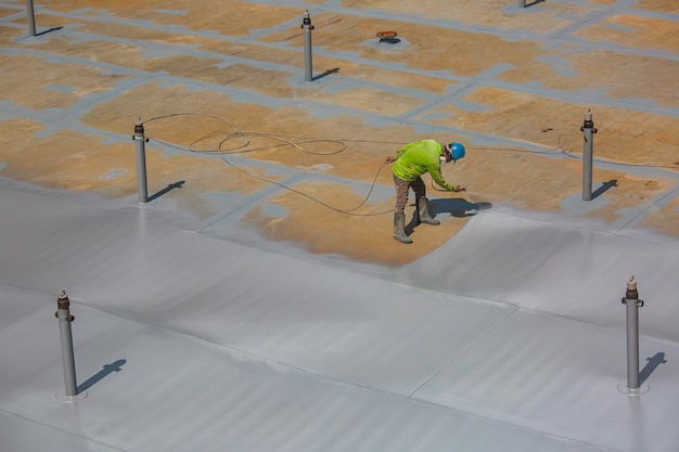 Trabalhador masculino de vista superior segurando uma pistola de pulverização industrial usada para a superfície do tanque da placa do telhado na pintura e revestimento industrial de aço