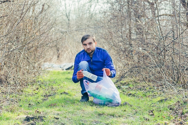 Trabalhador masculino do parque coleta lixo e plástico na floresta na primavera e cuida do solo e das árvores