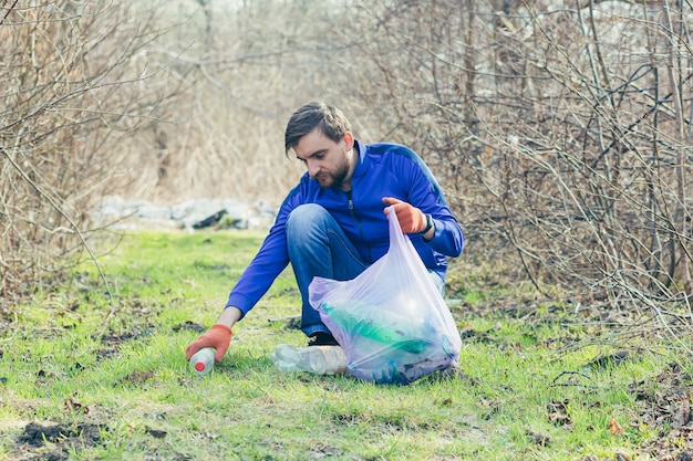 Trabalhador masculino do parque coleta lixo e plástico na floresta na primavera e cuida do solo e das árvores