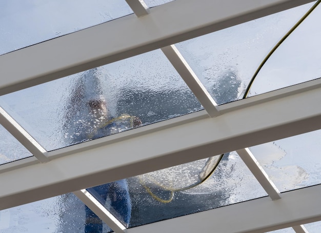 Trabalhador masculino lavando grande extensão de telhado de vidro sobre piscina com tubo de mangueira