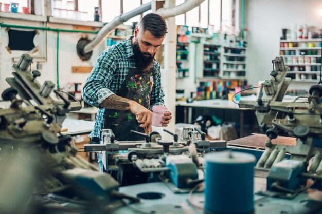 Trabalhador masculino pressionando tinta no quadro enquanto usa a máquina de impressão em uma oficina