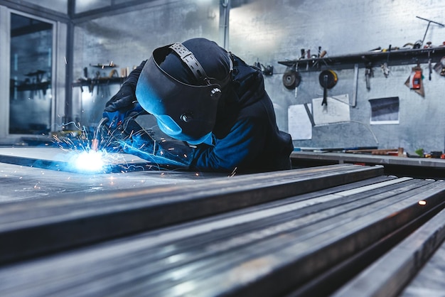 Trabalhador masculino usando capacete e luvas soldando construção de aço na fábrica Tiro horizontal