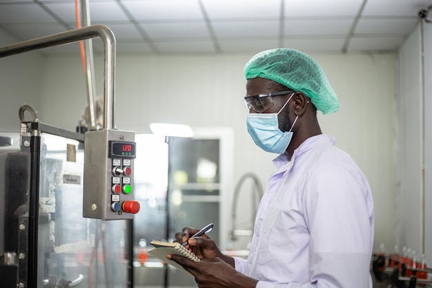 Trabalhador negro afro-americano inspecionando produto de bebida em máquinas de fábrica de engarrafamento