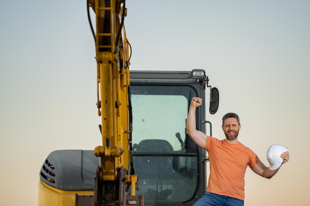 Trabalhador no canteiro de obras Construtor no capacete Homem da construção com capacete Trabalhador na construção com capacete Trabalhador da indústria no prédio da construção Construtor no prédio do canteiro com escavadeira