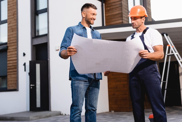 Trabalhador no capacete segurando a planta perto do homem e construindo ao ar livre