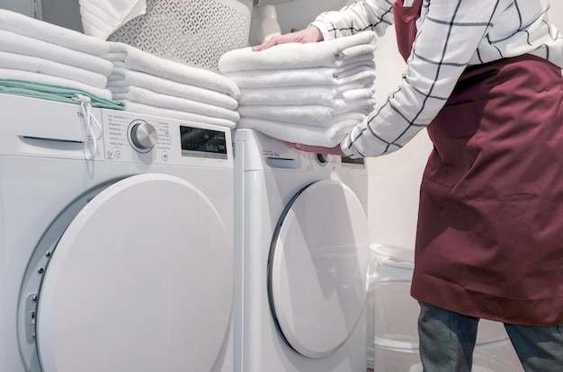 Trabalhador no hotel tem muitas toalhas nas mãos perto da máquina seca na lavanderia