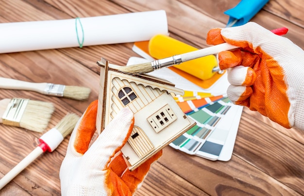 Trabalhador pinta modelo de casa sobre a mesa com pincéis, livro de amostras de cores e rolo de pintura Conceito de melhoria da casa