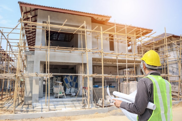 Foto trabalhador profissional de engenharia e arquitetura com capacete de proteção e papel de planos no local de construção de uma casa